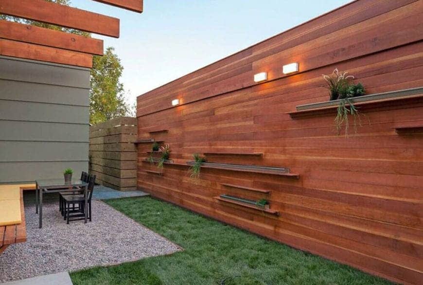 小后院设有现代化的水平木制围栏板，带有浮动的植物架子和l形草坪。