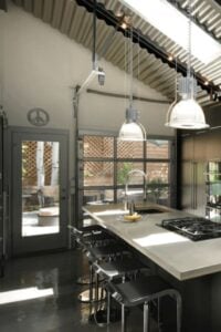 Industrial-style厨房功能暗色调和波纹金属天花板。两个圆顶吊坠灯吊在天花板上,也在自然采光天窗画。