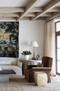 正式的客厅设有毛绒家具和大面积地毯，自然光线从窗户射入。裸露的横梁与天花板齐平。设计:Andrew Howard Interior Design