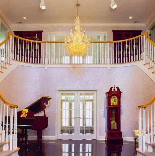 用腮红图案壁纸设计的分叉楼梯，还有一个落地式大钟和钢琴。它装有一扇法式门，由一盏可爱的枝形吊灯照亮。