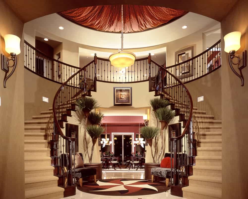 华丽的住宅展示了覆盖着米色地毯的红木楼梯。它由圆形天花板上悬挂的枝形吊灯和巨大的烛台照亮。