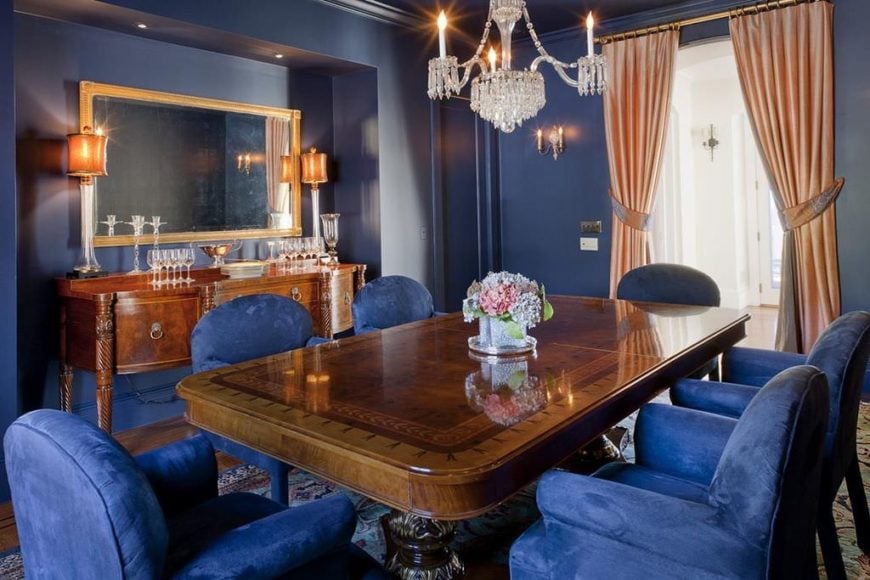 维多利亚风格的餐厅有六把电动蓝紫色椅子，一个长方形的木桌，玻璃吊灯，和传统的地毯。