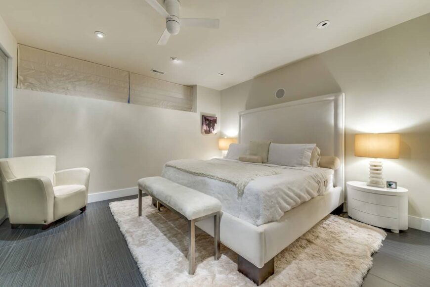 可爱的奶油色主卧室，有软垫床和重音椅。床脚处有一条长凳，与床上用品和蓬松的地毯相映成趣。