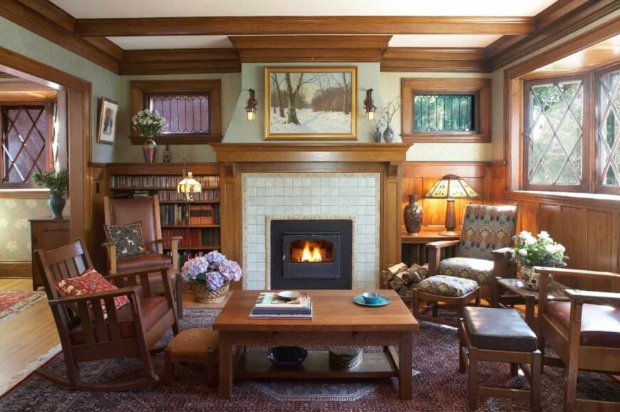 工匠风格的客厅，壁炉旁边有一个嵌壁式书架，壁炉安装在白色瓷砖墙上。它有木制的椅子和凳子搭配一个木制的中心桌子。