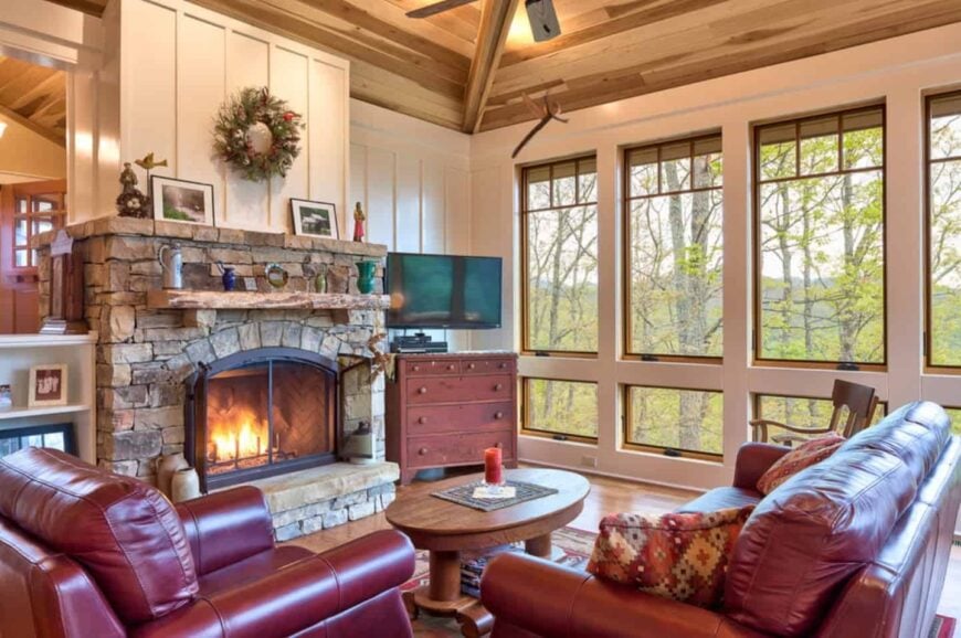 工匠风格的客厅，配有红色皮革沙发和木制咖啡桌，正对着石头壁炉。它有拱形的木质天花板和玻璃窗，可以俯瞰壮观的山景。