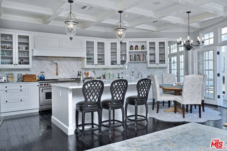 白色带点黑色的厨房，玻璃吊灯挂在格子天花板上，大理石后挡板，白色橱柜，黑色硬木地板，还有一个带三把黑色椅子的早餐岛。
