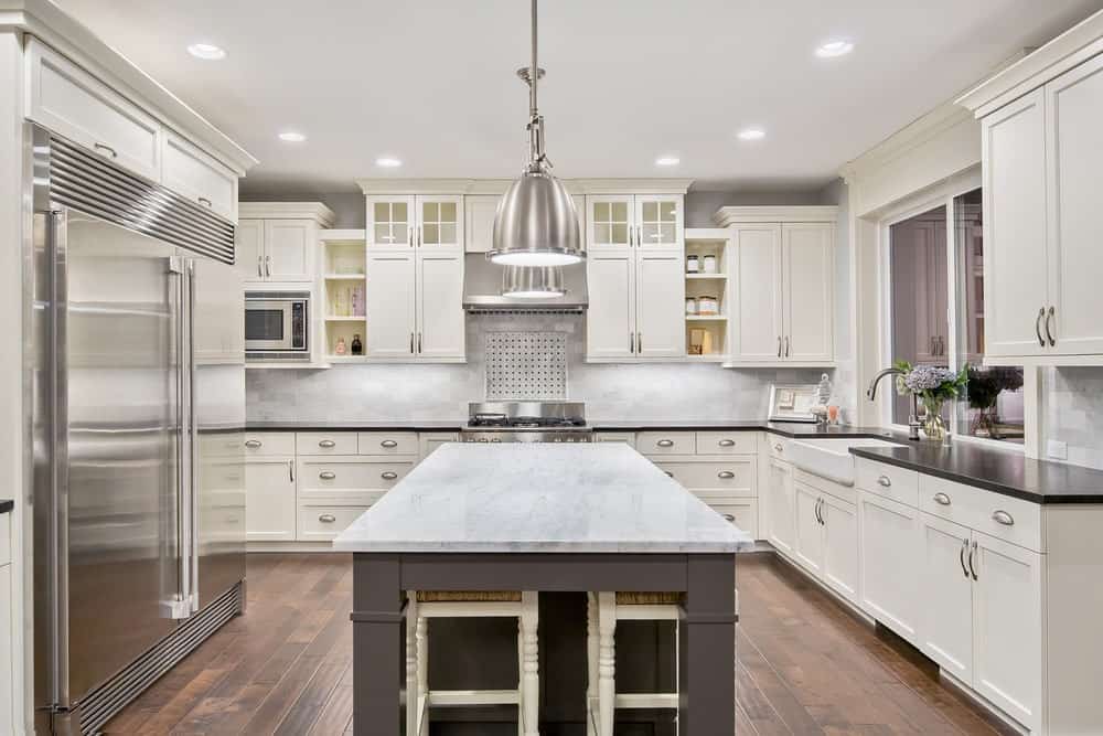 现代厨房，硬木地板，白色橱柜，不锈钢电器，带大理石台面的岛式桌子和两盏铝制吊灯。