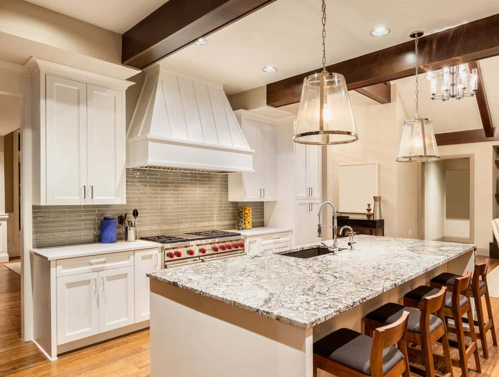 舒适的厨房，大理石台面岛桌，带靠垫的木椅，白色橱柜，硬木地板和两盏大玻璃吊灯。