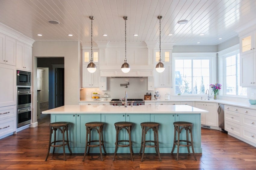 一个时尚的厨房，有一个浅水色的早餐岛，木椅，不锈钢电器和悬挂的球形吊灯。