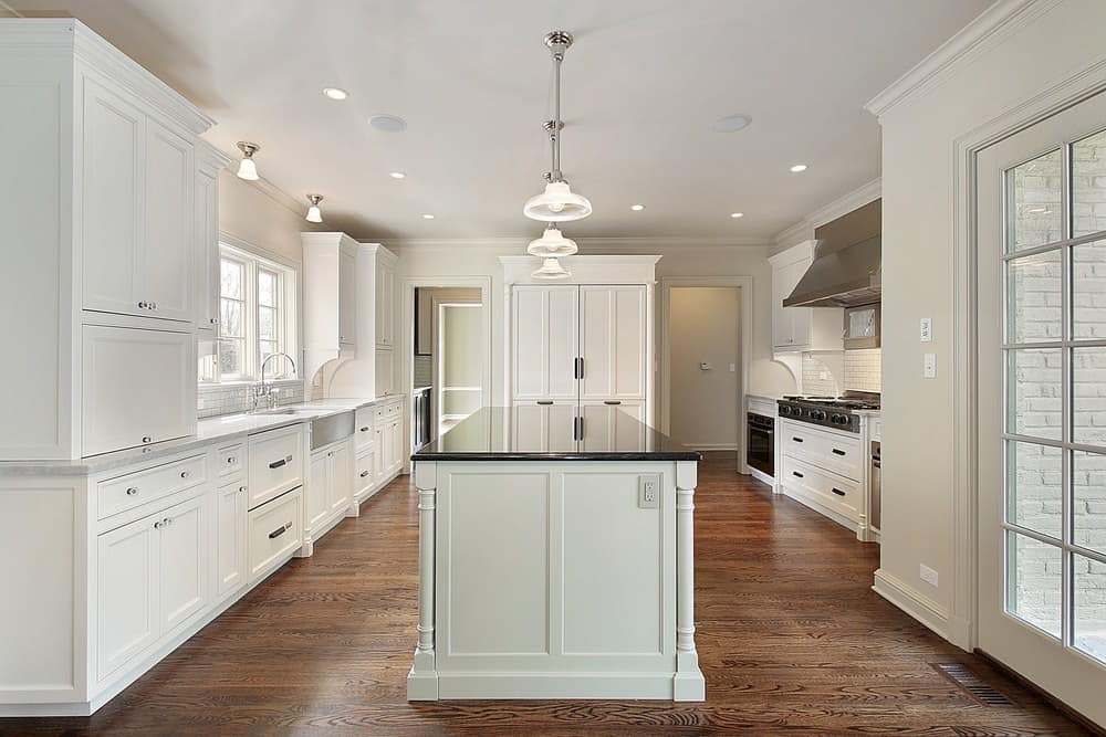 干净的厨房，硬木地板，白色橱柜，带黑色大理石台面的岛式桌子和玻璃吊灯。