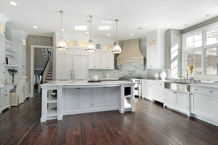 经典的白色厨房里有木制橱柜、带大理石台面的岛式餐桌、吊灯和硬木地板，与白色元素形成对比。