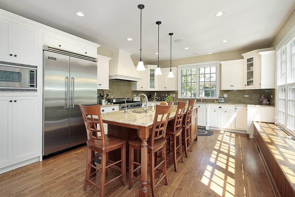 厨房里有硬木地板、白色橱柜、玻璃窗、带大理石台面的早餐岛桌、木椅和经典吊灯。