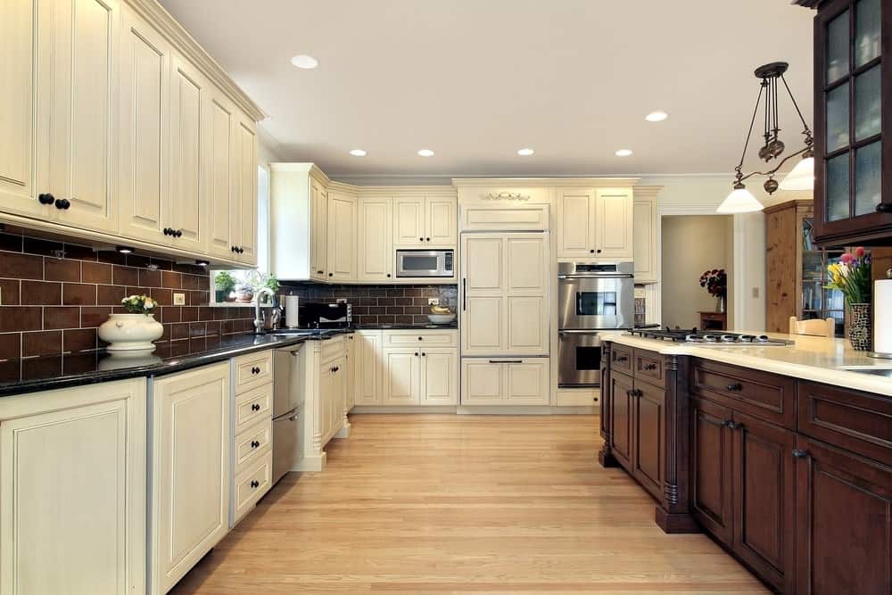 宽敞的厨房，棕色砖后挡板，硬木地板，白色木橱柜和复古吊灯和嵌入式照明。