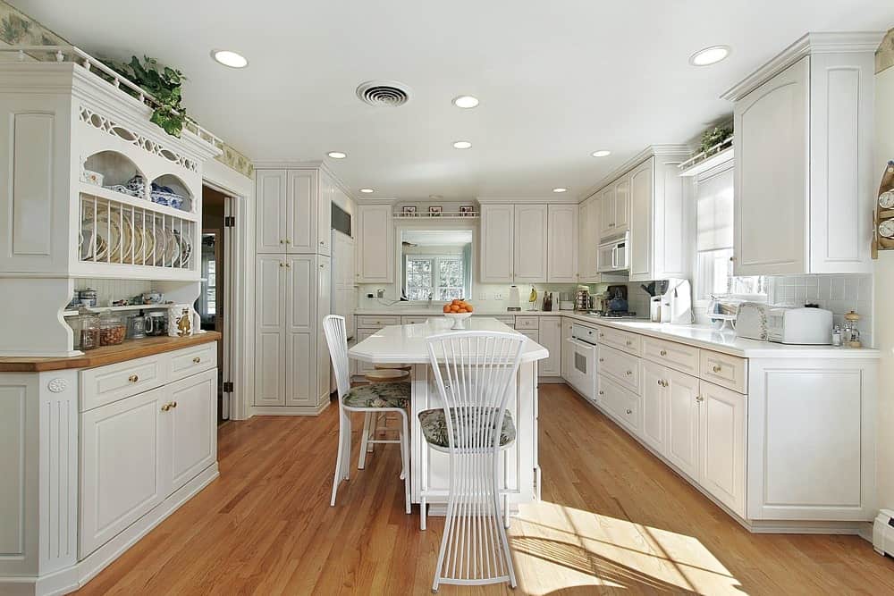 宽敞的厨房，白色木橱柜，硬木地板和白色早餐岛与椅子。