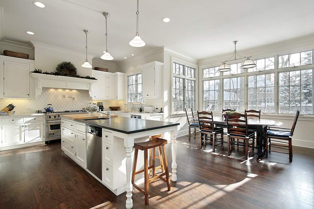 简单的厨房里有白色木柜、钻石图案的白色后挡板、银色吊灯和一个带水槽的厨房岛台、白色橱柜和一把木椅。