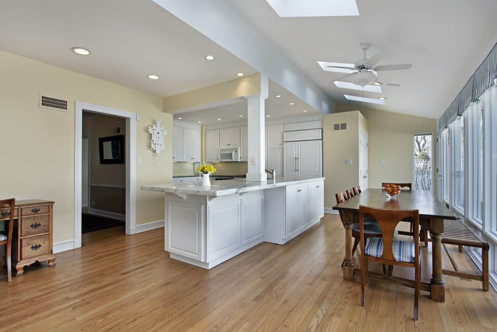 厨房有奶油色的墙壁，白色的木柜，大理石台面，硬木地板和白色的墙壁装饰。