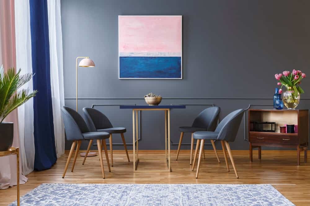 蓝灰色的墙壁与抽象的墙壁艺术画布完美地匹配了窗帘。它有一张四人用餐的小餐桌，放在硬木地板上。