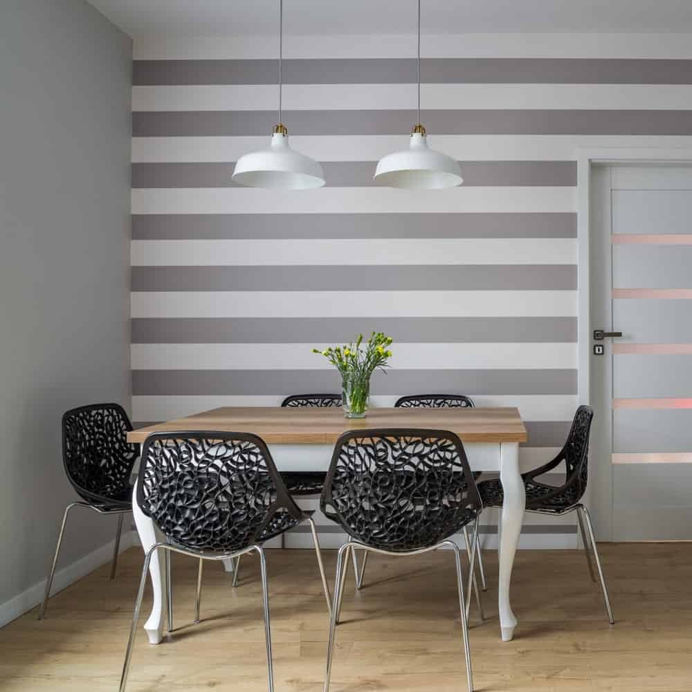 光滑的餐厅强调灰色条纹醒目的墙壁和黑色华丽的椅子周围的木餐桌。白色天花板上挂着一对白色吊坠，照亮了房间。