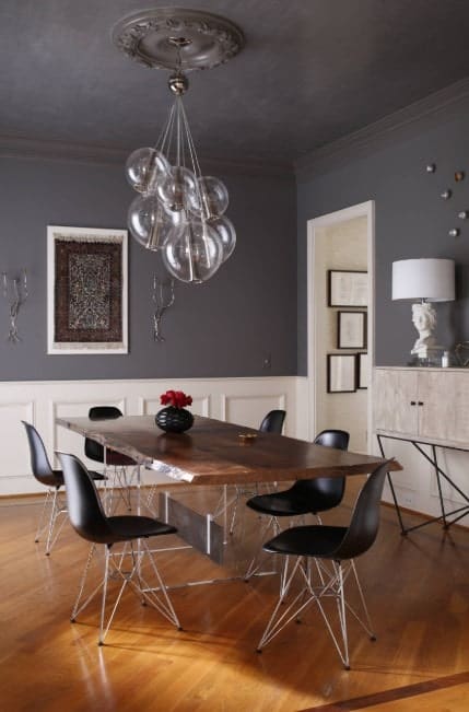 一盏闪烁的枝形吊灯悬挂在天花板上，上方是长方形的餐桌和黑色的椅子。它有灰色的墙壁，白色的护墙板和硬木地板。