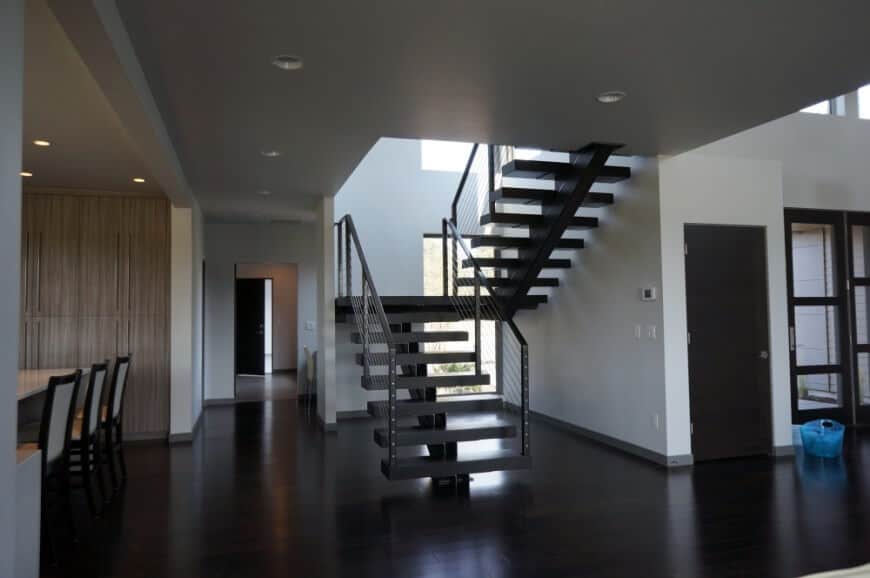 黑色半旋转楼梯，单根细钢栏杆与白墙和硬木地板相衬。
