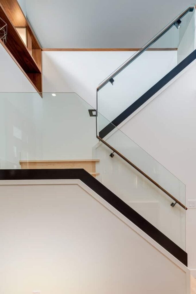 奶油色的半转弯楼梯展示了无框玻璃栏杆和木制扶手，并在白色墙壁上踩着踏板。
