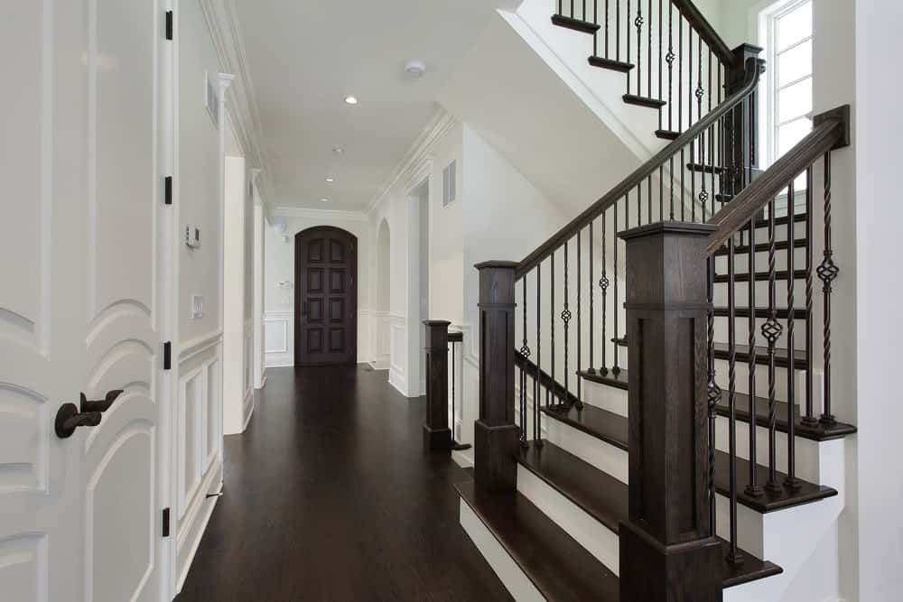 优雅的半转弯楼梯，深棕色华丽的栏杆与踏板相匹配。它与硬木地板和白墙形成了统一的外观。