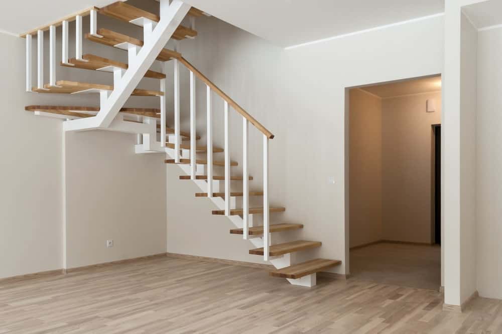 半旋转楼梯，白色直单桁和主轴，木制踏板和栏杆与白墙和硬木地板互补。