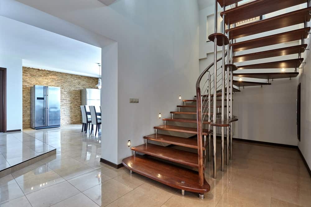 一个优雅的弧形半转弯楼梯与开放踏面和不锈钢栏杆。它由安装在白墙上的楼梯灯照明。