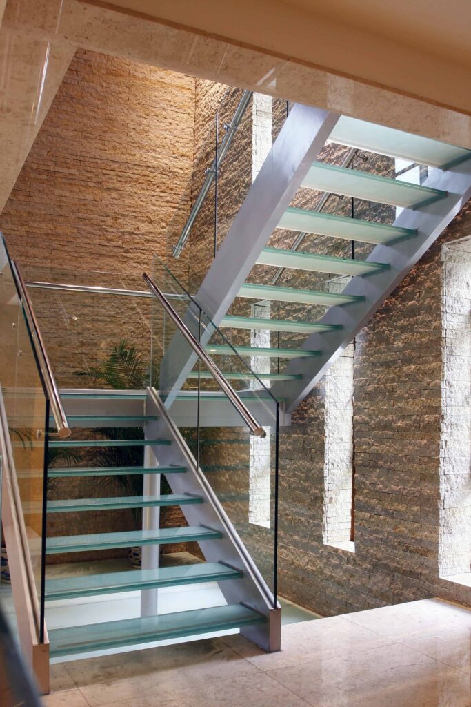 砖墙环绕着钢化玻璃开立楼梯，楼梯采用不锈钢扶手和木制横梁。