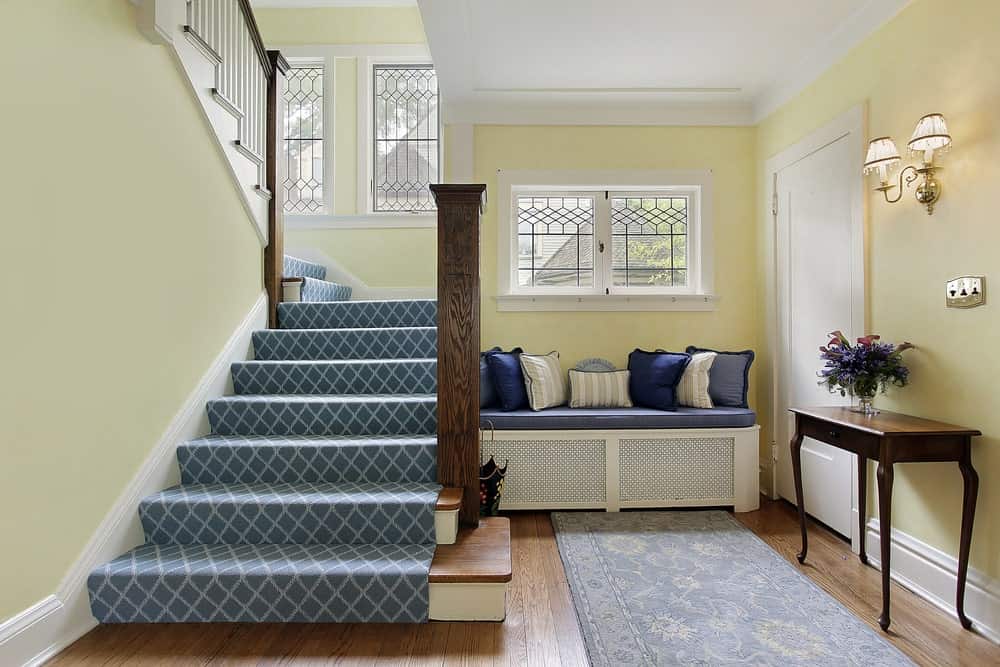 木制半转弯楼梯与海湾造型强调了一个可爱的蓝钻石图案的runner沿着前厅。