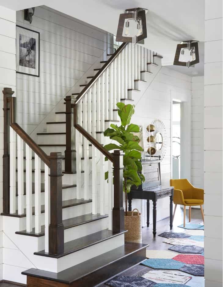 传统的楼梯有白色的立管和深色的木踏板，设计有无花果叶植物和多色几何地毯。