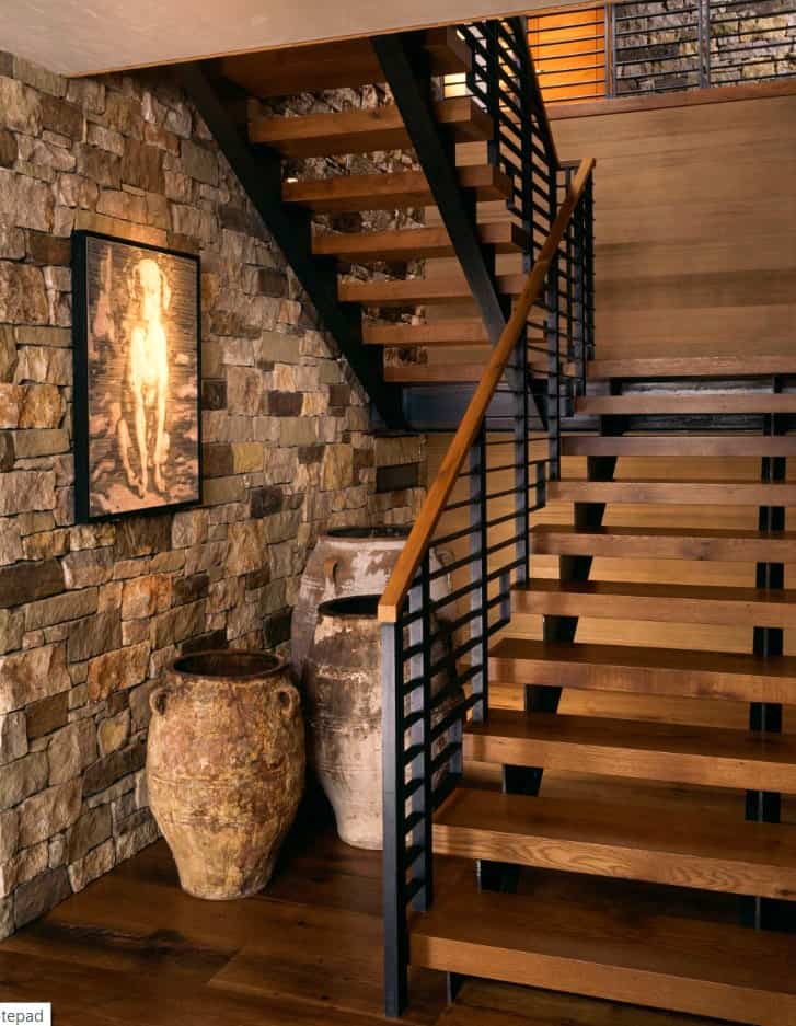现代的楼梯，锻铁栏杆和木制踏板，与墙壁和地板相匹配，以强调砖墙。下面的老式罐子创造了一种乡村的感觉。