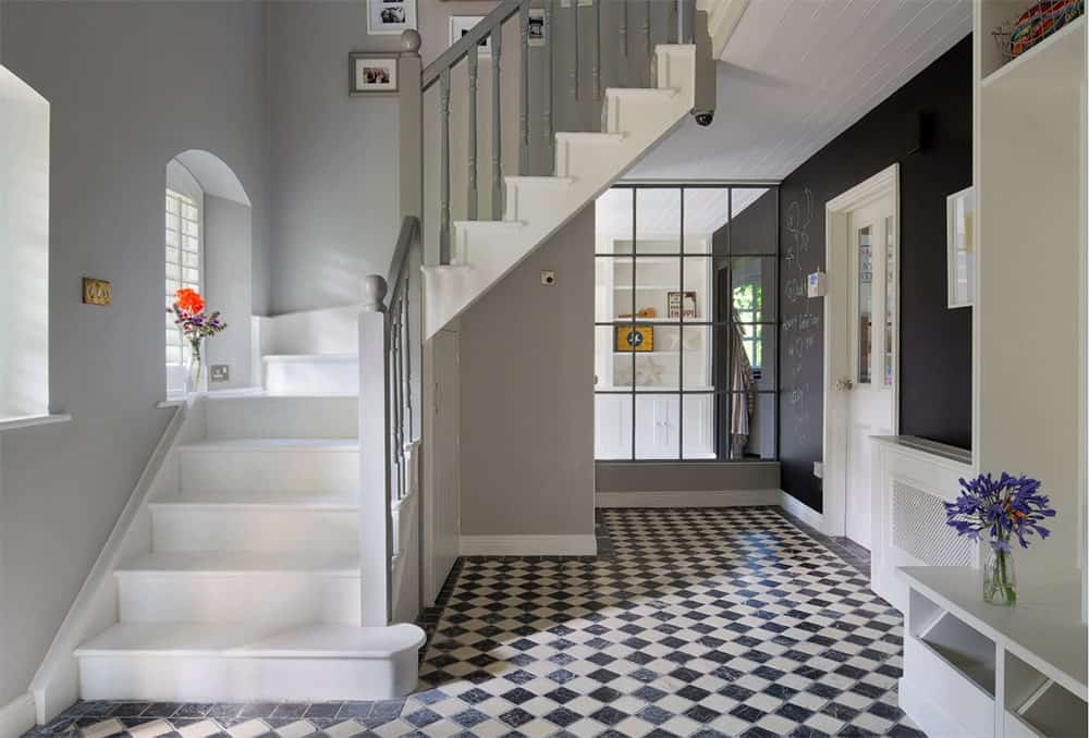 白色的半转弯楼梯配以黑白钻石图案的大理石瓷砖地板。它有灰色的木栏杆，下面有内置的储藏室。