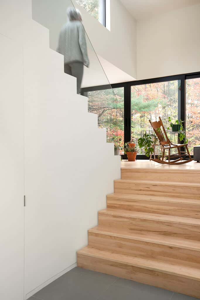天然木材半旋转楼梯的特点是无框玻璃栏杆对着白墙和玻璃窗。