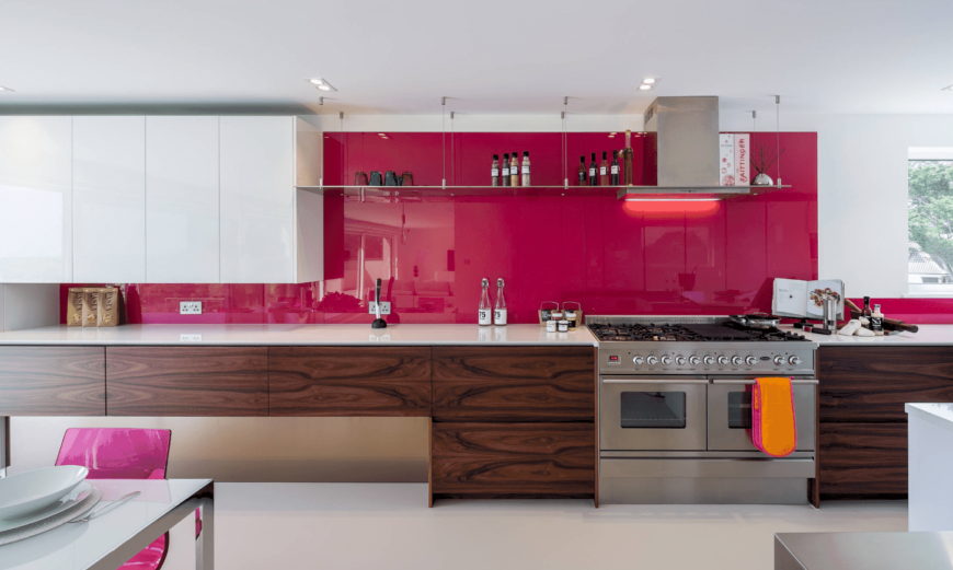 优雅的厨房由一个有光泽的洋红色后挡板突出。它有白色的上层橱柜和木材染色的下层橱柜，上面有白色的大理石柜台。