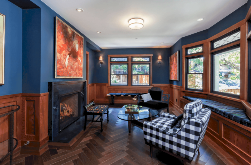 华丽的蓝色客厅设有半深色木护壁墙和人字纹硬木地板。它有一个内置的靠窗座位角落，配有蓝色软垫和黑白相间的格子椅子。