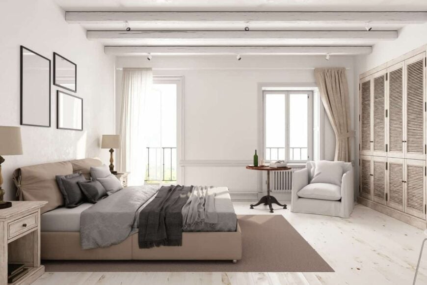 主卧室以白色墙壁和硬木地板为特色，与白色天花板和横梁相匹配。有一扇门通向房子的阳台。