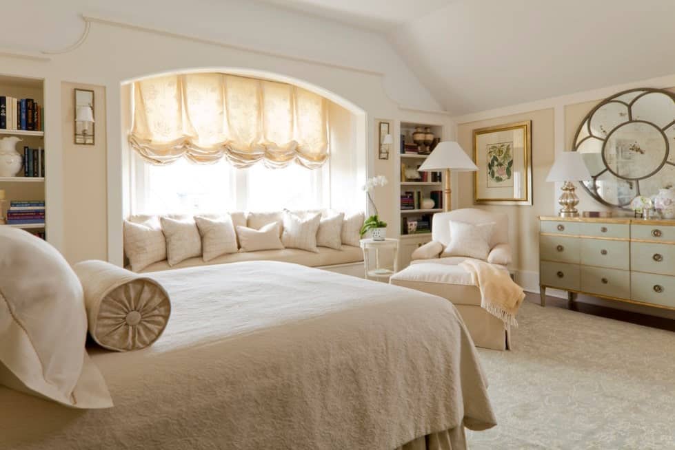 主卧室有一个大的经典地毯和米黄色的墙壁。房间提供一张舒适的床和一个阳光房区域，以及一把带边桌的椅子。