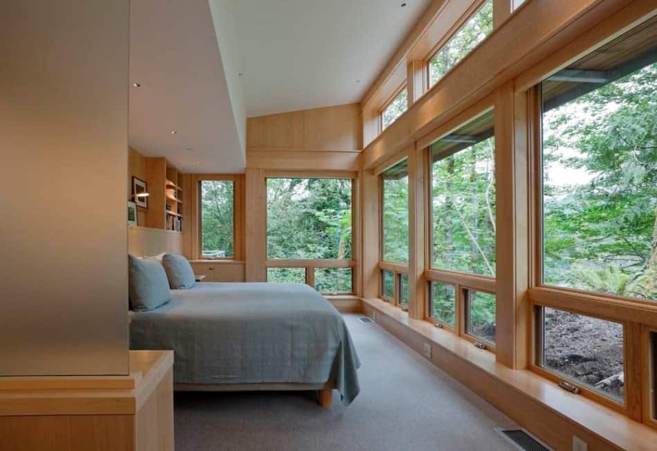 这间主卧室设有灰色地毯地板和一张大床。多扇玻璃窗俯瞰着宁静的环境。