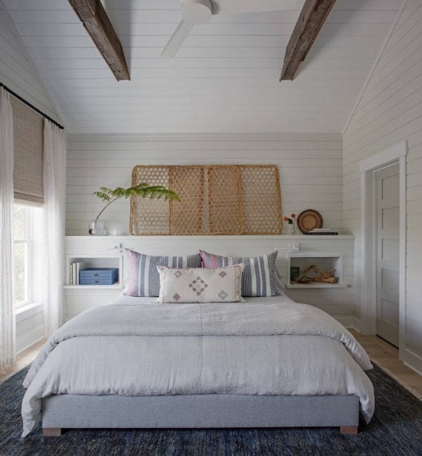主卧室有一个大灰色地毯和一张舒适的床。白色的墙壁与白色的天花板搭配着质朴的横梁。