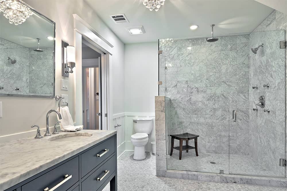 传统浴室设有一间步入式淋浴间，内有木凳和大理石瓷砖墙，毗邻一个带有灰色橱柜和大理石台面的梳妆台。