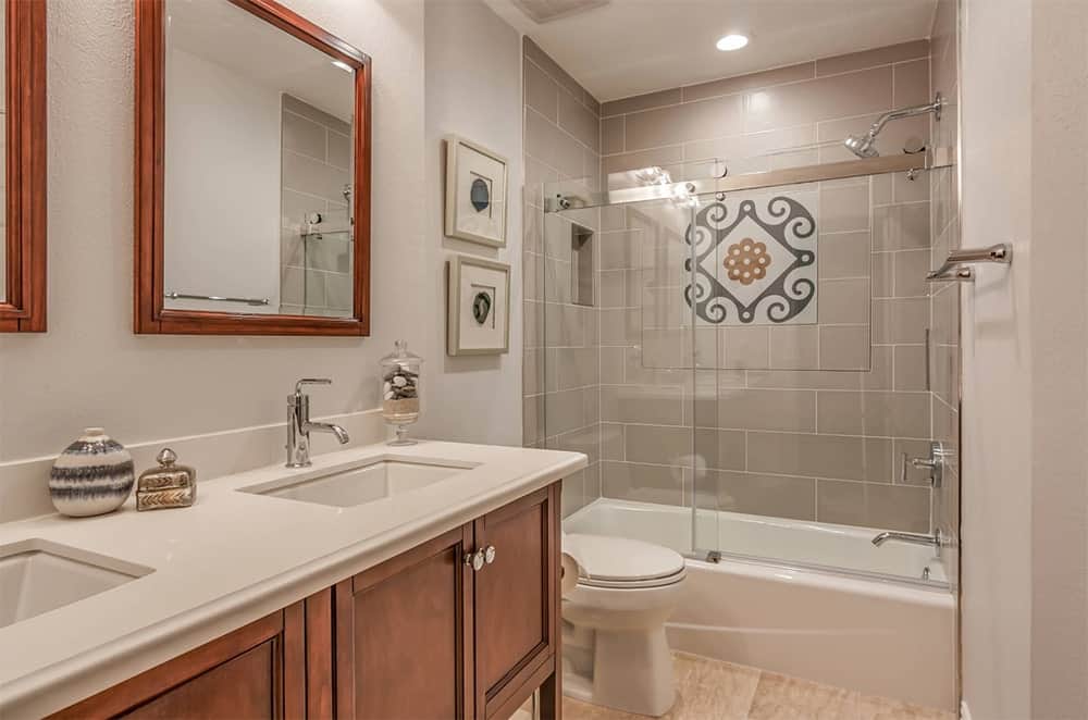 地中海式浴室设有一个带有木制橱柜的双洗手池，与镜子相匹配，还有一个步入式淋浴浴缸组合，由灰色地铁瓷砖墙突出。