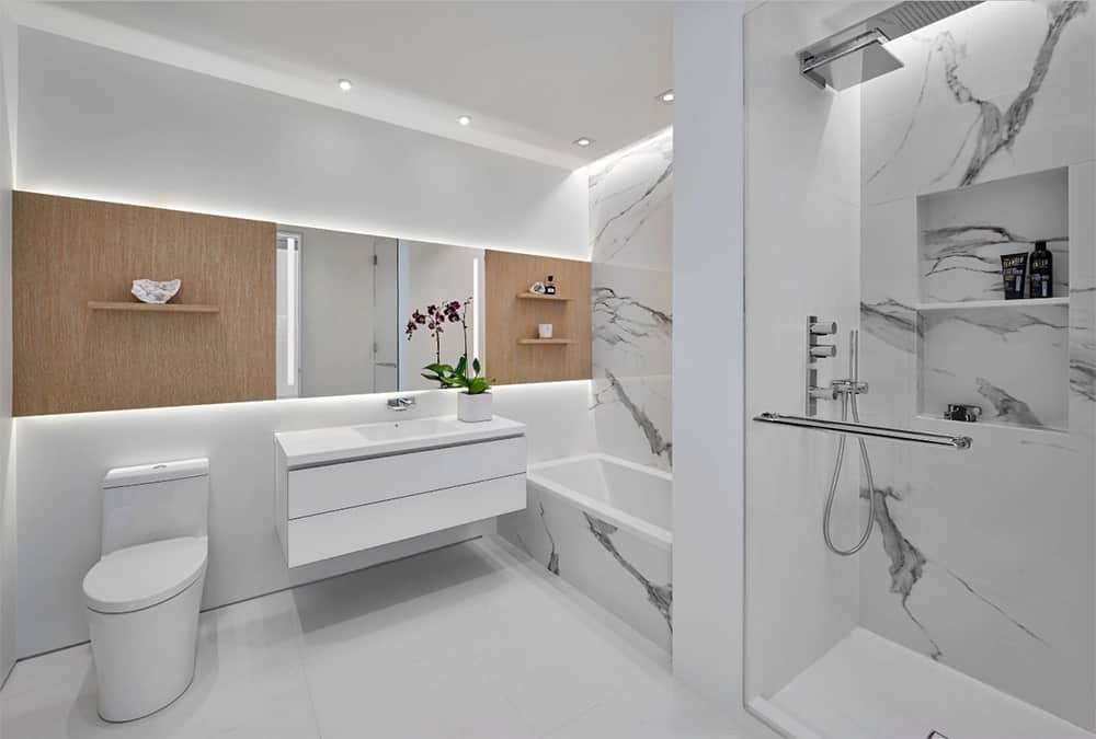 干净的白色浴室以木墙和架子为重点，浴缸和淋浴区配有白色大理石瓷砖。它还包括一个带有药柜镜子的浮动梳妆台。
