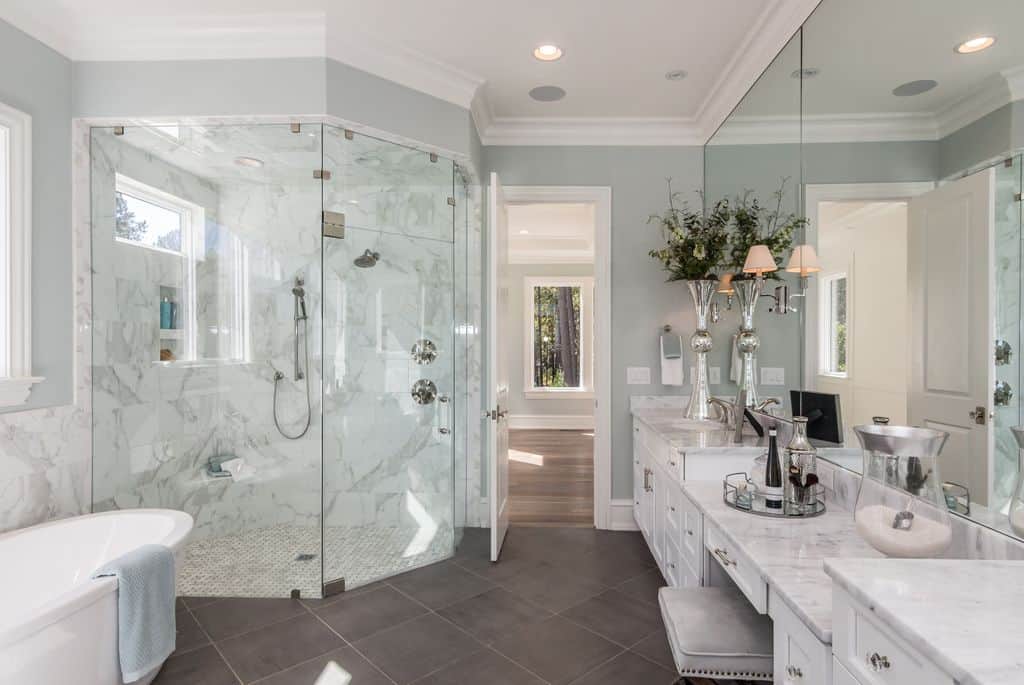 漂亮的灰色墙壁和白色的皇冠装饰为这个豪华的浴室增添了精致。它有一个带白色橱柜的长洗手池，浴缸旁边还有一间步入式淋浴房。