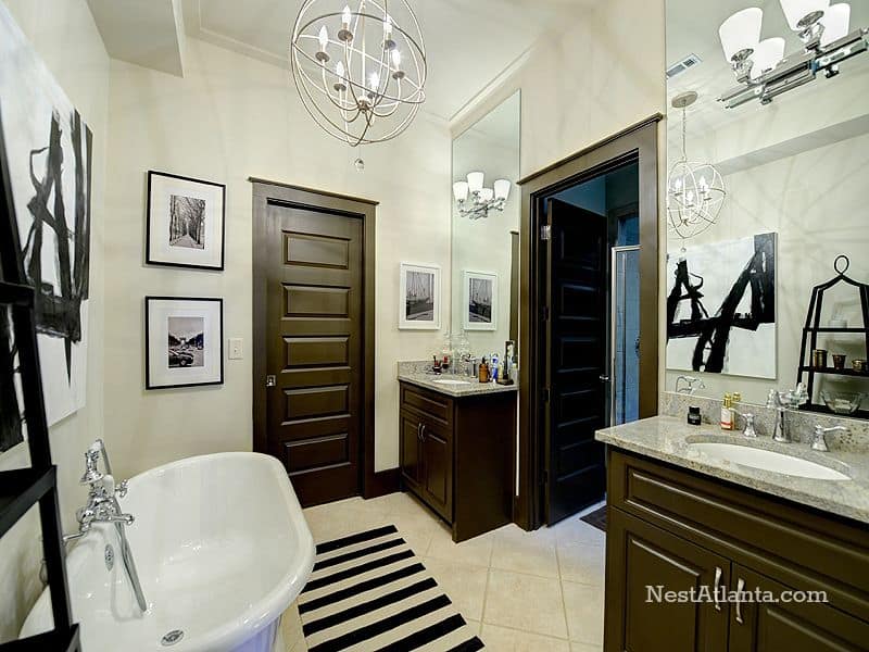 漂亮的黑白浴室设有一个工业球形吊灯，一对顶部为灰色大理石的盥洗台，一个独立的浴缸和条纹地毯与墙壁帆布和框架相辅相成。