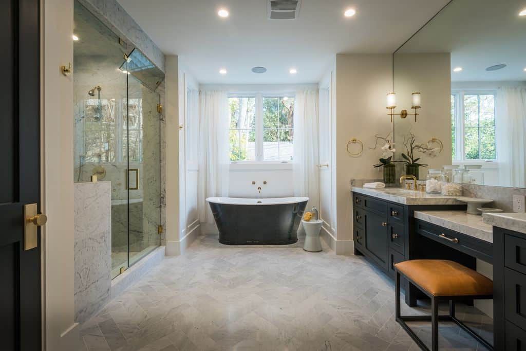 带黑色浴缸的优雅浴室与顶部铺有灰色大理石的洗手池上的黑色橱柜相得益彰。