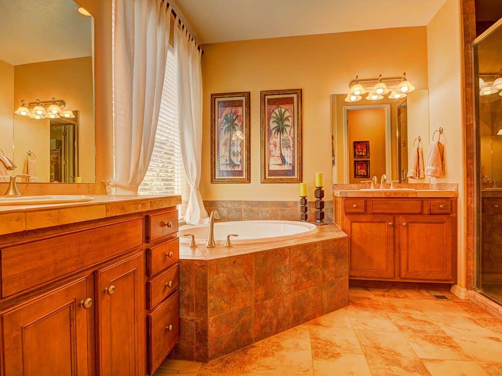 明亮的橙色浴室设有一个石浴缸，位于木制盥洗台的中央，由安装在无框镜子上的花式烛台照明。