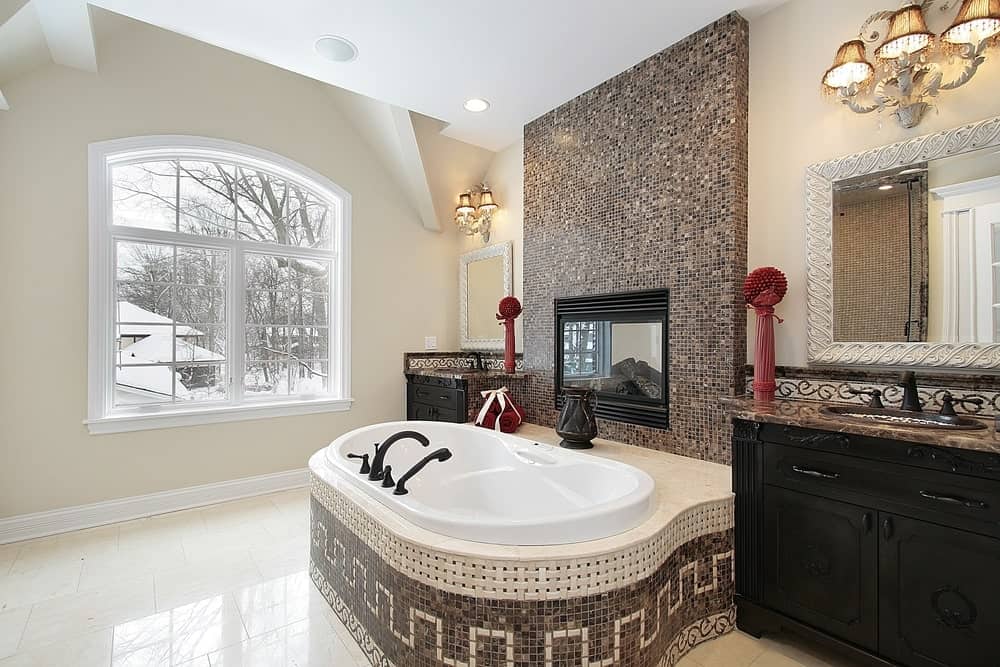 迷人的浴室设有固定在马赛克瓷砖墙上的浴缸。它位于黑色木盥洗台的中央，大理石台面和白色镜子，由花式壁灯照明。