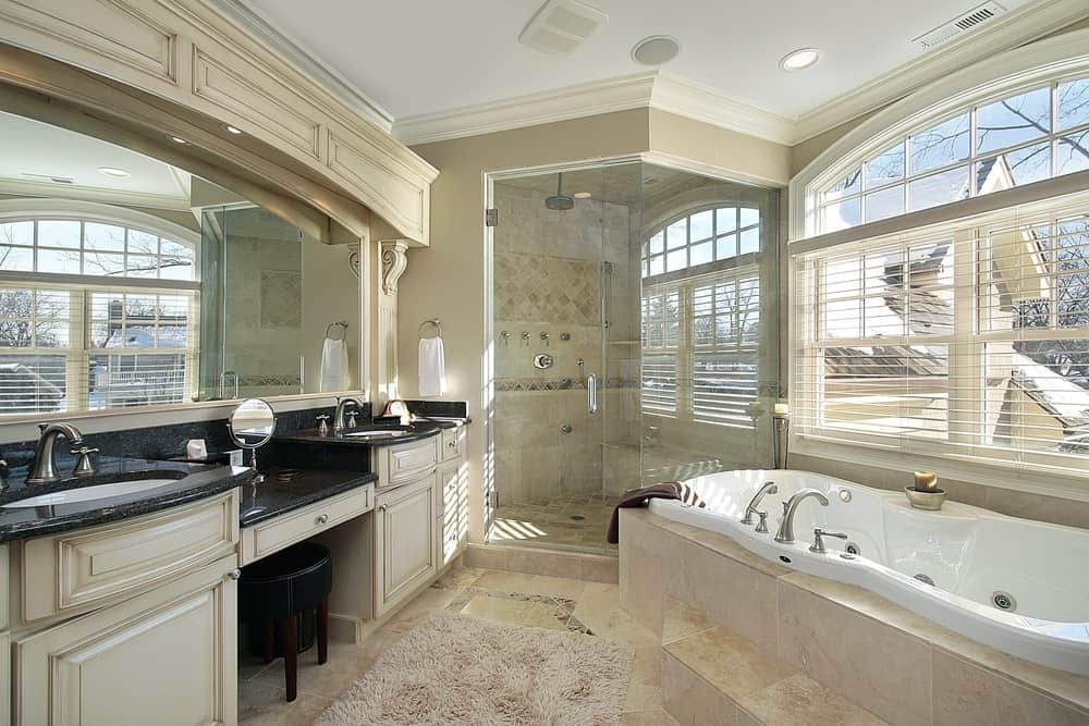经典的浴室，巨大的双水槽梳妆台顶部是黑色大理石，搭配黑色软垫凳子。它正对着固定在窗户下的浴缸，毗邻一间步入式淋浴间。