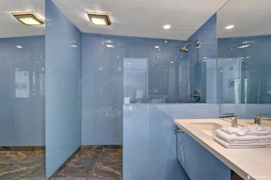 这间中世纪风格的主浴室拥有天蓝色的墙壁和时尚的瓷砖地板。它还有一个淋浴区和一个浮动洗手池。